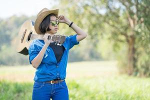 kvinna ha på sig hatt och bära henne gitarr i gräs fält foto