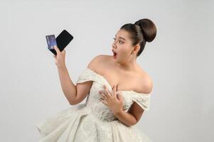 ung asiatisk skön brud inlägg med kreditera kort och smartphone i hand foto