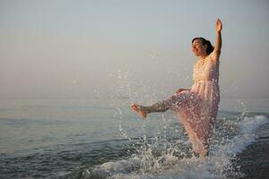 Lycklig medelålders kvinna i en klänning stänk vatten förbi de hav. foto