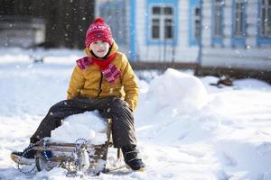 en liten rolig pojke rider på en trä- kälke i de by på en vinter- dag. foto