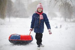 en pojke drar en rör kälke tvärs över de snö på en vinter- dag. foto