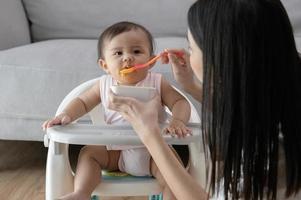 ung mor portion bebis äter blandning mat på bebis stol foto