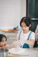 två liten söt asiatisk tjejer, inlärning på vilket sätt till göra bröd och bageri med en nyfiken och Lycklig leende ansikte. hon lär och spelar foto