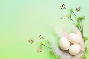 vita påskägg i ett känsligt bo av färgade fjädrar med utfällda bladknoppar på grenarna. våren, en religiös högtid, livets födelse. kopieringsutrymme. ljusgrön bakgrund foto