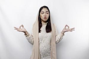 asiatisk muslim kvinna praktiserande yoga och mediterar utgör med stängd ögon isolerat förbi vit bakgrund foto