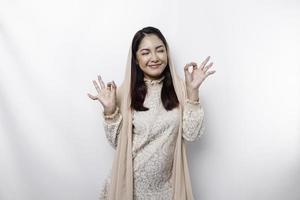 porträtt av en leende asiatisk muslim kvinna, ger ett ok hand gest isolerat över vit bakgrund foto