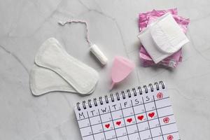 menstruations- kalender med sanitär servetter, tamponger, menstruations- kopp på vit bakgrund. begrepp av kritisk dagar, menstruation foto