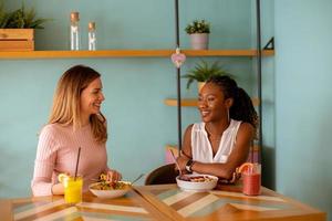 ung svart och caucasian kvinna har Bra tid, dricka färsk juicer och har friska frukost i de Kafé foto