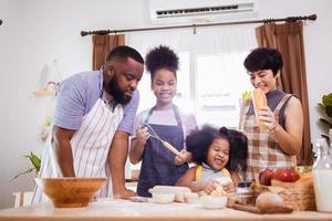 Lycklig afrikansk amerikan familj njut av tillsammans medan förbereda de mjöl för framställning småkakor på Hem foto
