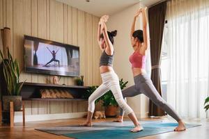 asiatisk kvinna och liten flicka praktiserande yoga från yoga uppkopplad kurs via smart TV på Hem foto