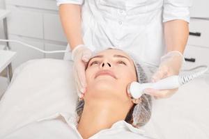 kosmetolog gör ultraljud hud åtdragning för föryngring kvinna ansikte använder sig av fonofores foto