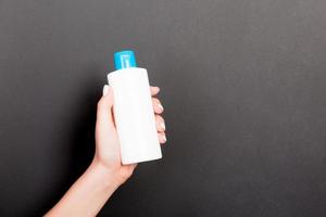 kvinna hand innehav grädde flaska av lotion isolerat. flicka ge rör kosmetisk Produkter på svart bakgrund foto