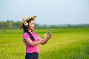 asiatisk kvinna jordbrukare innehav läsplatta gående i ris fält till Lagra information foto