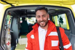 manlig läkare leende in i kamera, ambulans besättning arbetssätt, suddig på bakgrund foto