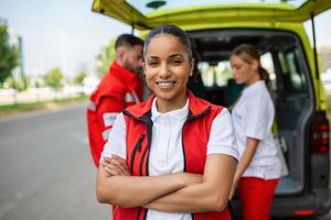 ung kvinna afrikansk amerikan para stående bak- av de ambulans. paramedics förbi de ambulans. två paramedics tar ut strecher från ambulans foto