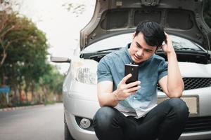 asiatisk man som använder mobiltelefon ringer efter hjälp efter ett bilhaveri på gatan. koncept av fordonsmotorproblem eller olycka och nödhjälp från professionell mekaniker foto