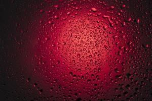 vatten droppar på glas på en röd bakgrund. foto