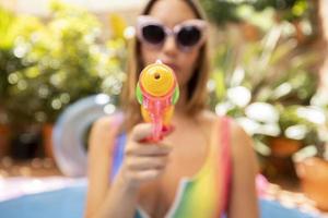 en Söt kvinna i bikini med en vatten pistol i en paddling slå samman foto