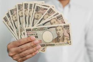 man hand innehav japansk yen sedel stack. tusen yen pengar. japan kontanter, beskatta, lågkonjunktur ekonomi, inflation, investering, finansiera och handla betalning begrepp foto