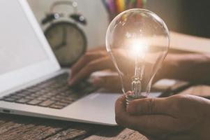 en person som håller en glödlampa bredvid en bärbar dator, nya idéer koncept foto