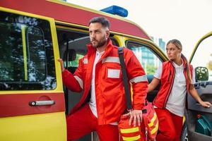 para sjuksköterska och nödsituation läkare på ambulans med utrustning. en sjukvårdare, stående på de bak- av ett ambulans, förbi de öppen dörrar. foto