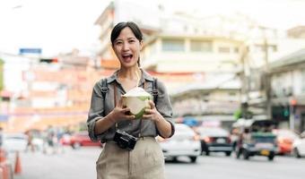 Lycklig ung asiatisk kvinna ryggsäck resande dricka en kokos juice på Kina stad gata mat marknadsföra i Bangkok, thailand. resande kontroll ut sida gator. foto