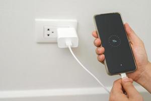 stänga upp hand plugging adapter avgift de batteri med utlopp uttag plugg och håll mobil telefon på vägg ,elektrisk säkerhet begrepp foto