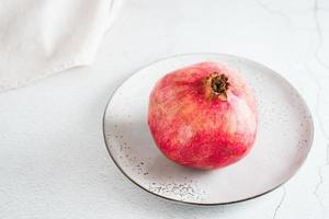 en hela mogen granatäpple på en tallrik på en ljus tabell. organisk naturlig mat. närbild foto