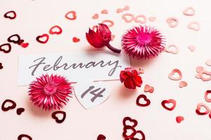 hjärtans dag. datum av februari 14 och torr blommor på en rosa bakgrund översållad med hjärtan. närbild foto