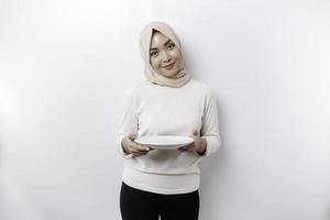 en leende asiatisk muslim kvinna är fasta och hungrig och innehav och pekande till en tallrik foto