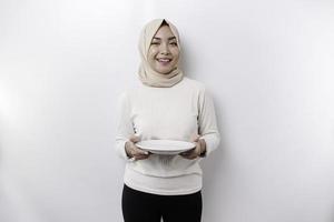 ett asiatisk muslim kvinna är fasta och hungrig och innehav en tallrik medan ser åt sidan tänkande handla om Vad till äta foto