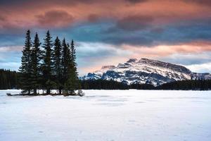 två domkraft sjö med montera runda och tall skog i vinter- på de kväll på banff nationell parkera foto