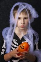 liten pojke i de halloween Spindel webb innehav ett orange boll. foto