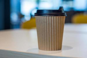 varm kaffe i brun papper kopp, kaffe i vit skrivbord, hämtmat kaffe i Kafé affär, på fläck bakgrund foto