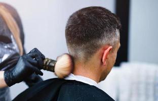 en frisör med säkerhet åtgärder för covid19, innehar sax i hans händer och nedskärningar en man, social distans, skärande hår med sudd handskar foto