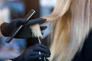 en frisör i sudd handskar innehar en par av sax och en hårkam. kvinna få en ny frisyr. foto