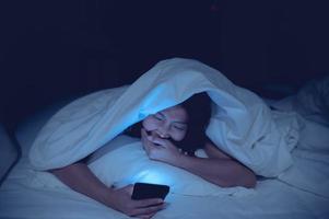 asiatisk kvinna spelar spel på smartphone i de säng på natt, thailand människor, missbrukare social media foto