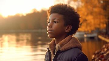 ung stilig afrikansk amerikan pojke stående nära de tyst sjö i de morgon- Sol - generatvie ai. foto