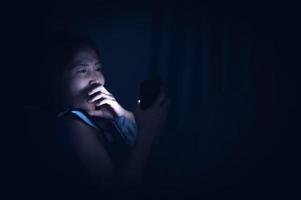 asiatisk kvinna spela smartphone i de säng på natt, thailand människor foto