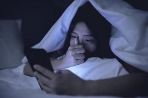 asiatisk kvinna spela smartphone i de säng på natt, thailand människor foto