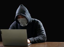 hacker spionera man ett person i svart luvtröja Sammanträde på en tabell ser dator bärbar dator Begagnade logga in Lösenord ge sig på säkerhet till cirkulera data digital i internet nätverk systemet, natt mörk bakgrund. foto