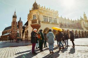 Krakow, Polen, 2023 - guide med Turné grupp promenad tillsammans i huvud fyrkant i krakow. fri turist gående turer med lokalbefolkningen. st.mary basilika. xiii århundrade krakow fyrkant foto