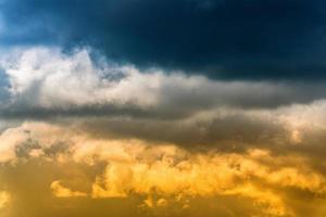 dramatisk blå åskmoln på topp och gul-gyllene fluffig moln upplyst förbi strålar av Sol på Nedan. fantastisk se naturlig meteorologi bakgrund foto