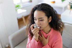 asiatisk kvinna använder sig av inhalator medan lidande från astma på Hem. ung kvinna använder sig av astma inhalator. närbild av en ung asiatisk kvinna använder sig av astma inhalator på Hem. foto