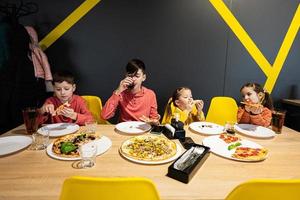 fyra barn äter italiensk pizza i pizzeria. barn äta på Kafé. foto