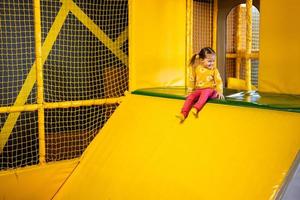 bebis flicka unge glida på gul lekplats parkera. barn i aktiva underhållning. foto