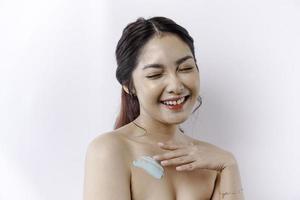 hud vård Produkter begrepp. asiatisk kvinna applicering fuktgivande lotion på kropp efter dusch, stående insvept i handduk, beskurna bild foto