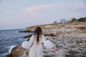 kvinna i vit klänning promenader på de strand stenar tillbaka se foto