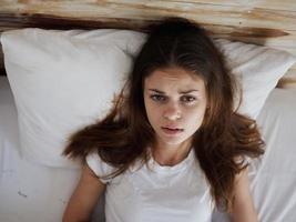 kvinna i en vit t-shirt lögner i säng känsla sjuk topp se foto