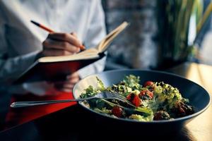 anteckningsblock med en penna i hand och sallad i en tallrik restaurang Kafé inskrift foto